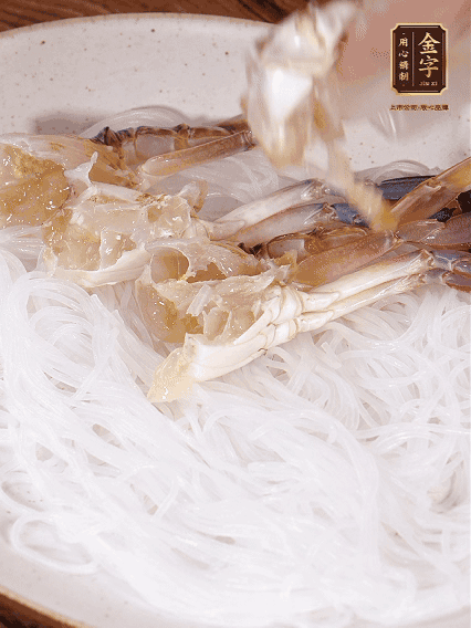 盤底墊上粉絲，擺上梭子蟹、火腿片，撒姜粒，淋上蒸魚豉油、花雕酒調味腌制15分鐘